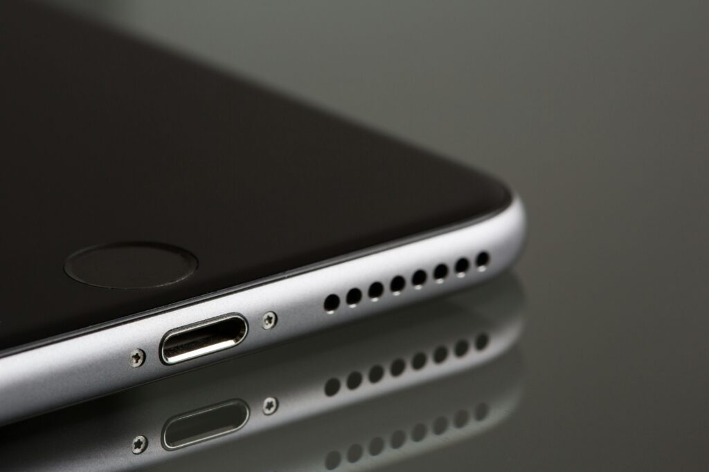 A sleek smartphone close-up highlighting its lightning connector and speaker, reflecting on a surface.