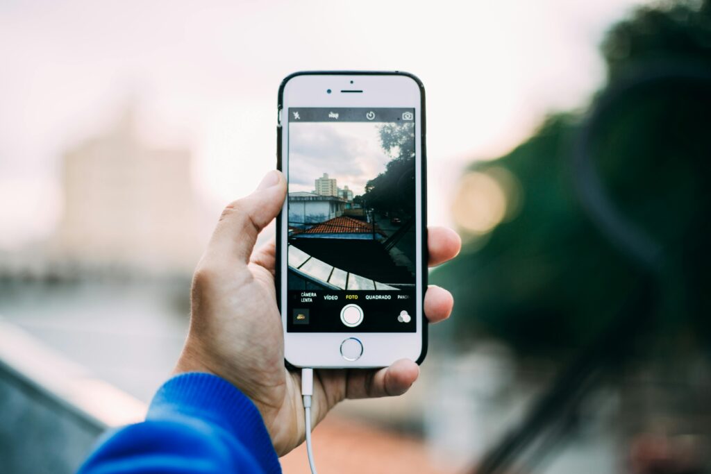 Close-up of a hand holding a smartphone while capturing a cityscape outdoors.